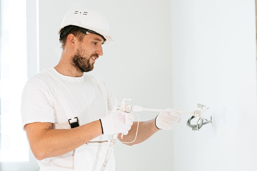 Électricien casqué fixant un câble sur un mur blanc avec des gants