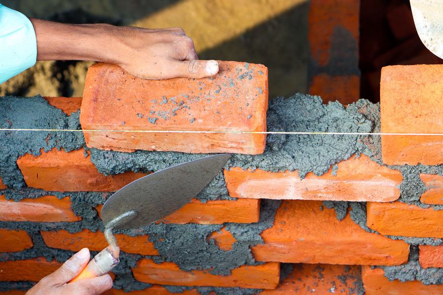 Mains posant une brique rouge sur un lit de mortier, avec une truelle, sur un mur en construction